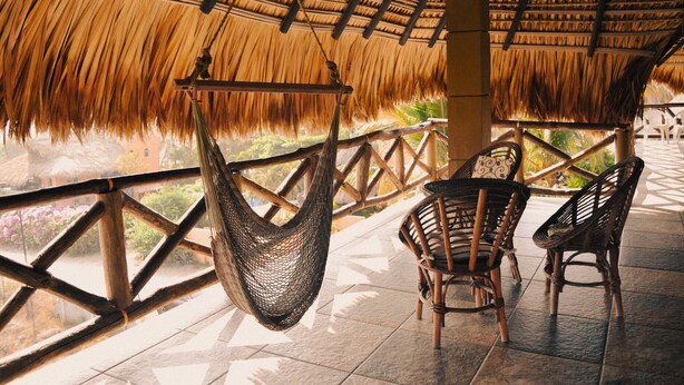 A covered outdoor seating area with woven chairs and a hanging hammock. - BeachfrontGuestHouse (5 Studios) (Puerto Escondido)