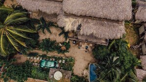 An aerial view of a resort with thatched-roof structures, a swimming pool, and lush tropical vegetation. - BeachfrontGuestHouse (5 Studios) (Puerto Escondido)