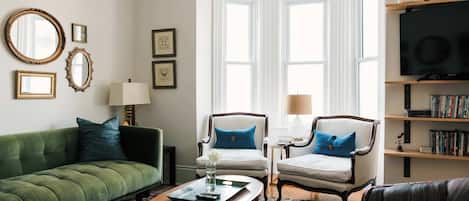 A living room with a green sofa, two armchairs, a coffee table, a TV, and a bookshelf.