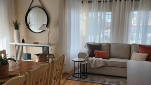 A cozy living room with a wooden dining table, chairs, a sofa, and a small side table.