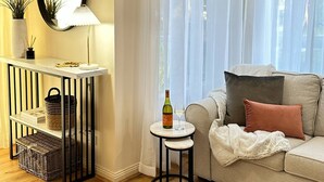 A living room with a sofa, a small table with a bottle and glass, a mirror, and a console table with baskets.
