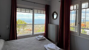 Ein Schlafzimmer mit einem großen Bett, zwei Pendelleuchten, Meerblick und einem mit Vorhängen drapierten Fenster.