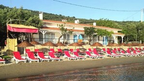 A beachside hotel with rows of red and white sun loungers, umbrellas, and a clear view of the sea.