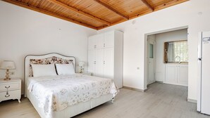 A bedroom with a wooden ceiling, a bed with a floral bedspread, white cabinets, and a window with a curtain.