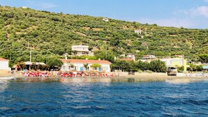 A coastal area with a beach, a row of beachside buildings, and a hillside in the background.
