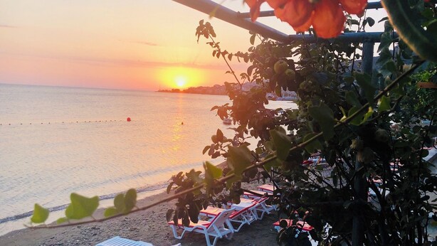 A beach with lounge chairs and a view of the sunset over the water.
