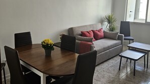 Ein Essbereich mit Holztisch und Stühlen, einer Couch mit Kissen und einem kleinen Beistelltisch.