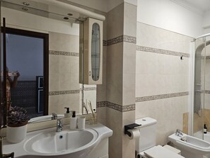 A bathroom with a sink, toilet, and bidet. There is a mirror above the sink and a towel rack on the wall.