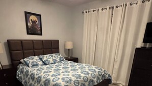 A bedroom with a bed, a ceiling fan, a nightstand, a lamp, a dresser, and a framed picture on the wall. - Charming 3-bedroom chalet with WiFi and AC in Kissimmee (Kissimmee)