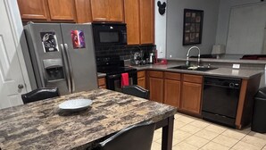 A kitchen with wooden cabinets, a granite countertop, a refrigerator, a microwave, a dishwasher, and a sink. - Charming 3-bedroom chalet with WiFi and AC in Kissimmee (Kissimmee)