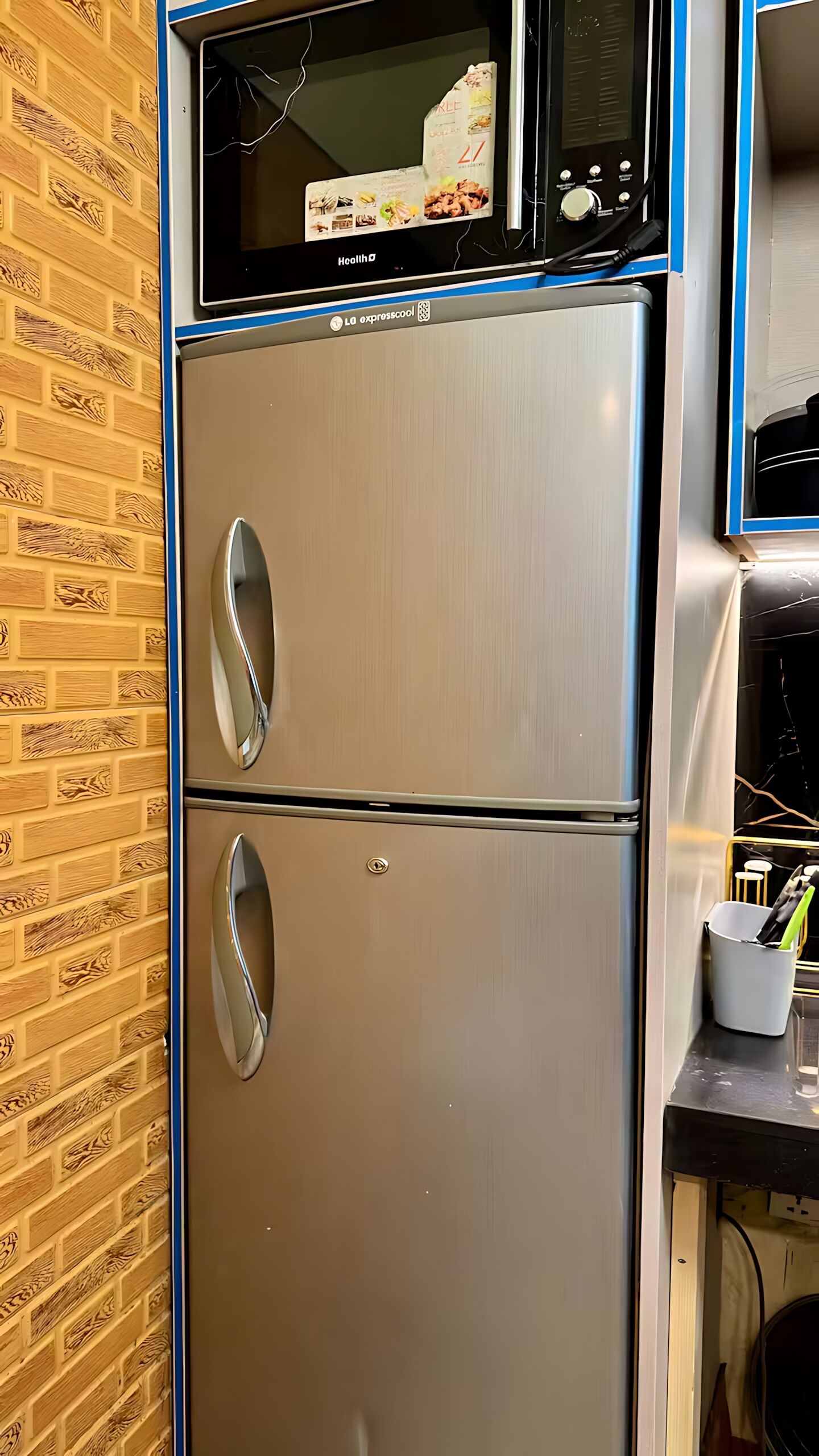 A stainless steel refrigerator with a built-in microwave on top, a digital display, and a freezer compartment below.