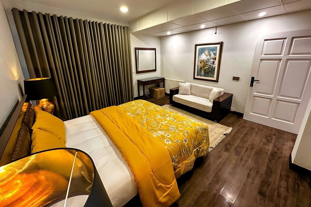 Habitación de hotel con cama, sofá, escritorio, lámpara, cuadro y puerta.
