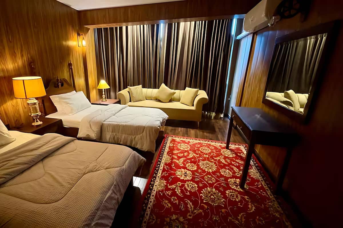 Habitación de hotel con dos camas, un sofá, un tapete rojo estampado y un espejo grande.