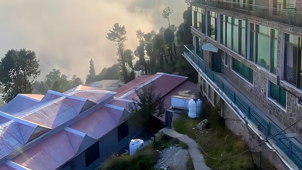 Un hotel moderno con techo plano y varios balcones con vistas a un paisaje brumoso.