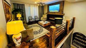 Una sala de estar con chimenea, televisor montado en la pared y una escalera con barandilla.