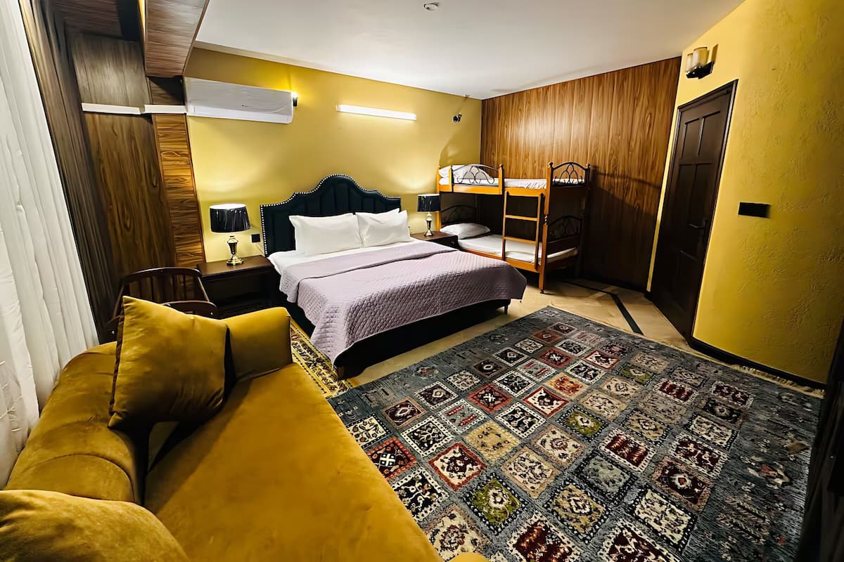 Una habitación de hotel con una cama, una cama individual apilada, un sofá, un tapete estampado y una pared de madera.