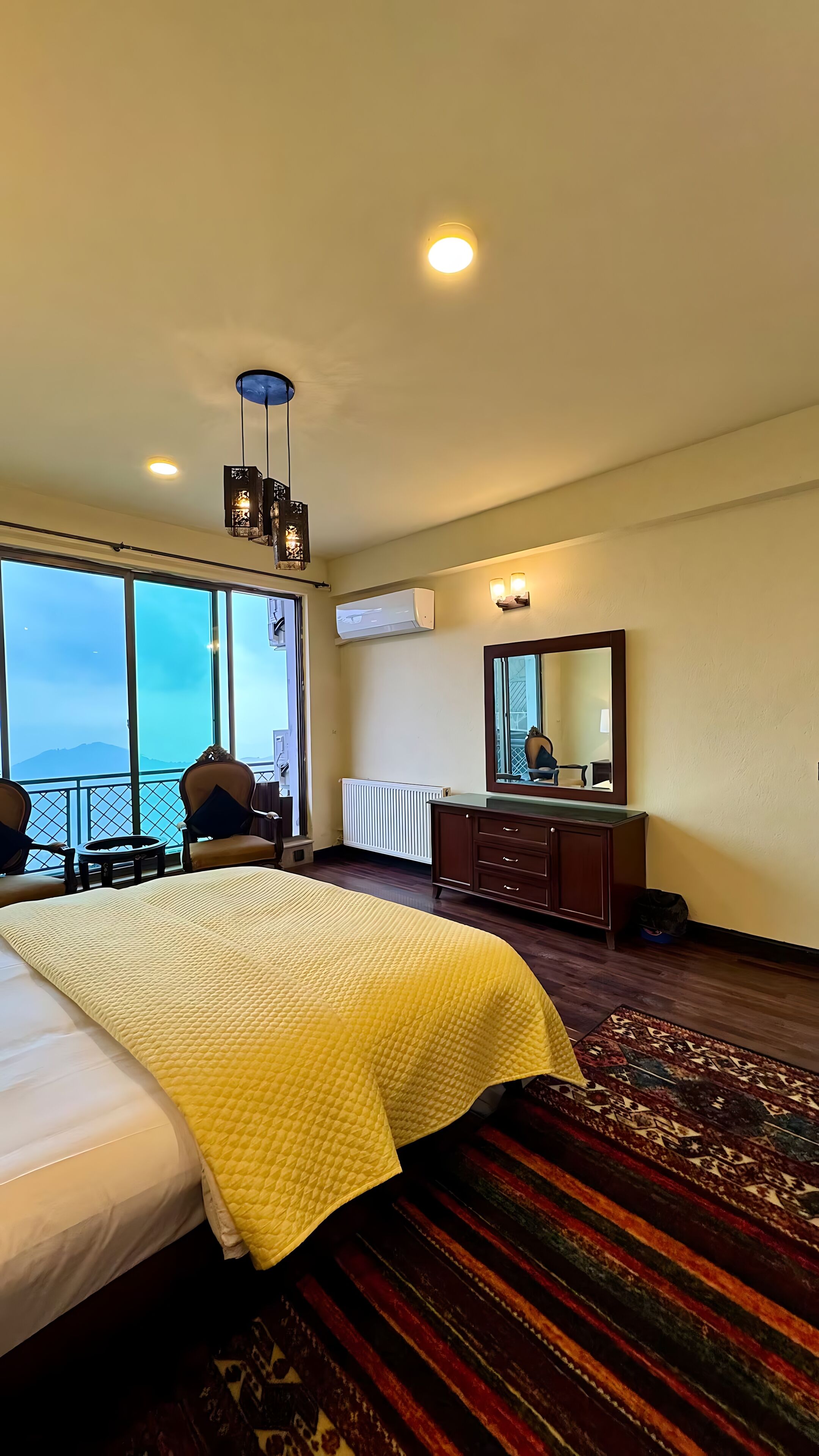 Una habitación de hotel con una cama grande, un aparador, un espejo y un balcón con vistas.