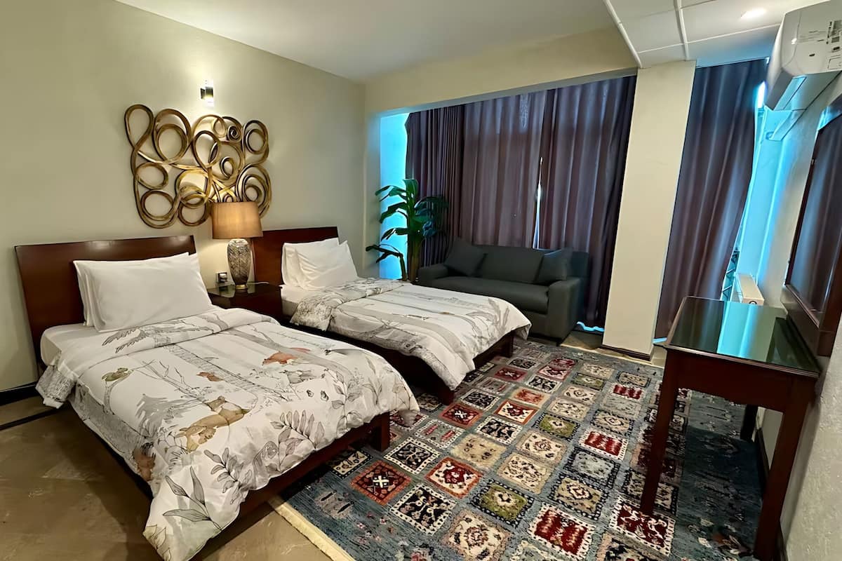 Habitación de hotel con dos camas, un sofá, un ventanal grande con cortinas, un adorno de pared y un televisor de pantalla plana.