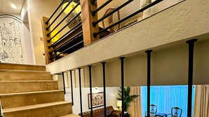 Un espacio habitable distribuido en varios niveles, con una escalera de madera, un sofá de cuero y un comedor con sillas.