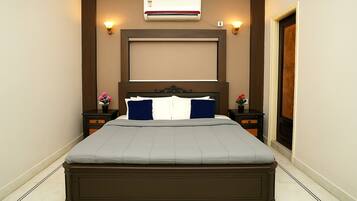 A bedroom with a large bed, two bedside tables, an air conditioning unit, and wall-mounted lights.