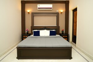 A bedroom with a large bed, two bedside tables, an air conditioning unit, and wall-mounted lights.