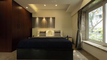 A modern bedroom with a large bed, built-in wardrobe, and a window with a view of greenery.