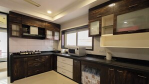 A modern kitchen with dark wood cabinets, a gas stove, a microwave, and a window providing natural light. - Victoria Apartment by Jadecaps (Kolkata)