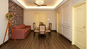 A dining area with a table set for four, a red sofa, and a vintage floor lamp. - Vivanta Apartment by Jadecaps (Kolkata)