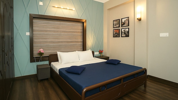 A neatly arranged bedroom with a bed, bedside tables, and a wall-mounted light fixture. - Vivanta Apartment by Jadecaps (Kolkata)