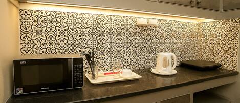 Una cocina con microondas, una bandeja con utensilios, una tetera blanca y un salpicadero decorativo.