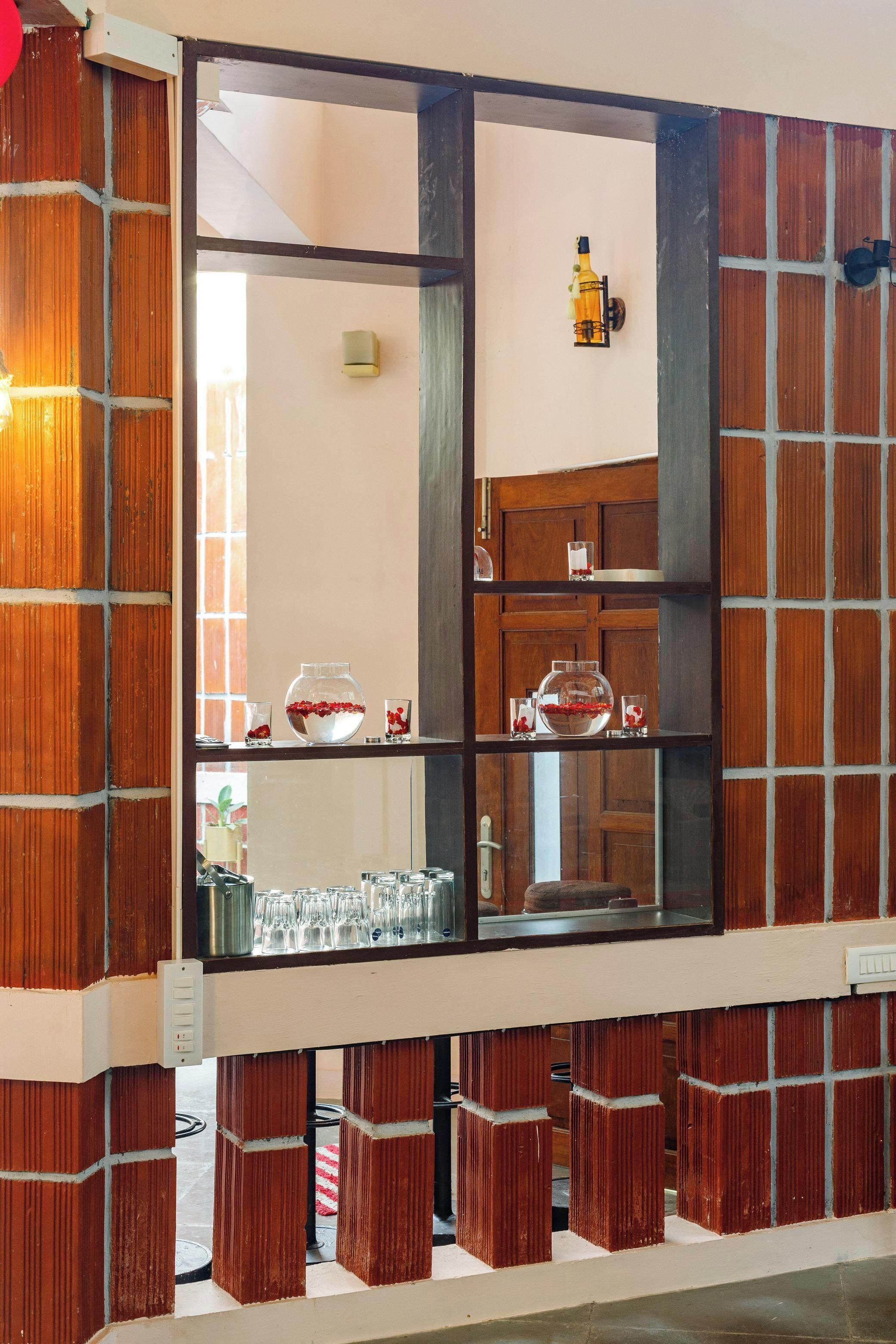 Een kamer met een metselwerk wand, een spiegel en planken met kristal en decoratieve objecten.