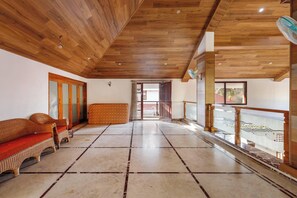 A spacious room with a high wooden ceiling, a large window, and a balcony with a decorative railing.