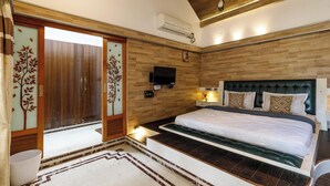 A bedroom with a large bed, wooden paneling, a flat-screen TV, and a sliding door with decorative glass panels. - Ananta Vilas by Stayjade (Bengaluru)