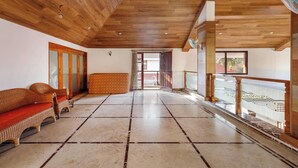A spacious room with a high wooden ceiling, a large window, and a balcony with a decorative railing. - Ananta Vilas by Stayjade (Bengaluru)