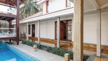 A poolside area with a pool, a covered seating area, and a building with a tiled roof and wooden doors.