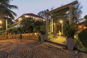 A well-lit entrance with a cobblestone pathway leading to a building with a red roof. - Ananta Vilas by Stayjade (Bengaluru)