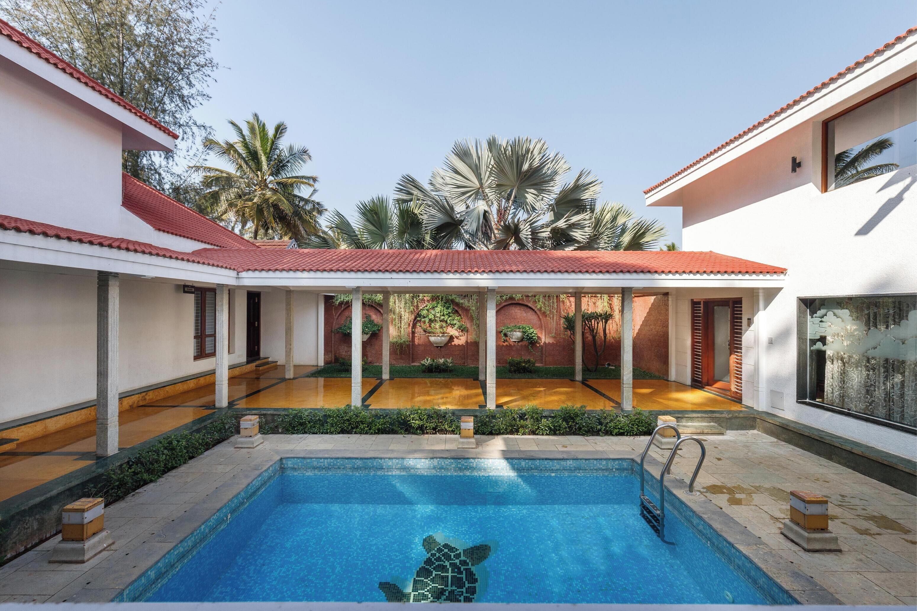A swimming pool with a turtle mosaic, surrounded by a covered patio with palm trees and a wooden deck.