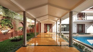 A covered corridor with a pool on the right, columns, and a brick wall with greenery. - Ananta Vilas by Stayjade (Bengaluru)