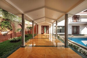 A covered corridor with a pool on the right, columns, and a brick wall with greenery. - Ananta Vilas by Stayjade (Bengaluru)