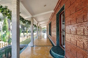 Um corredor coberto com colunas, uma parede de tijolos e vista para o verde lá fora.