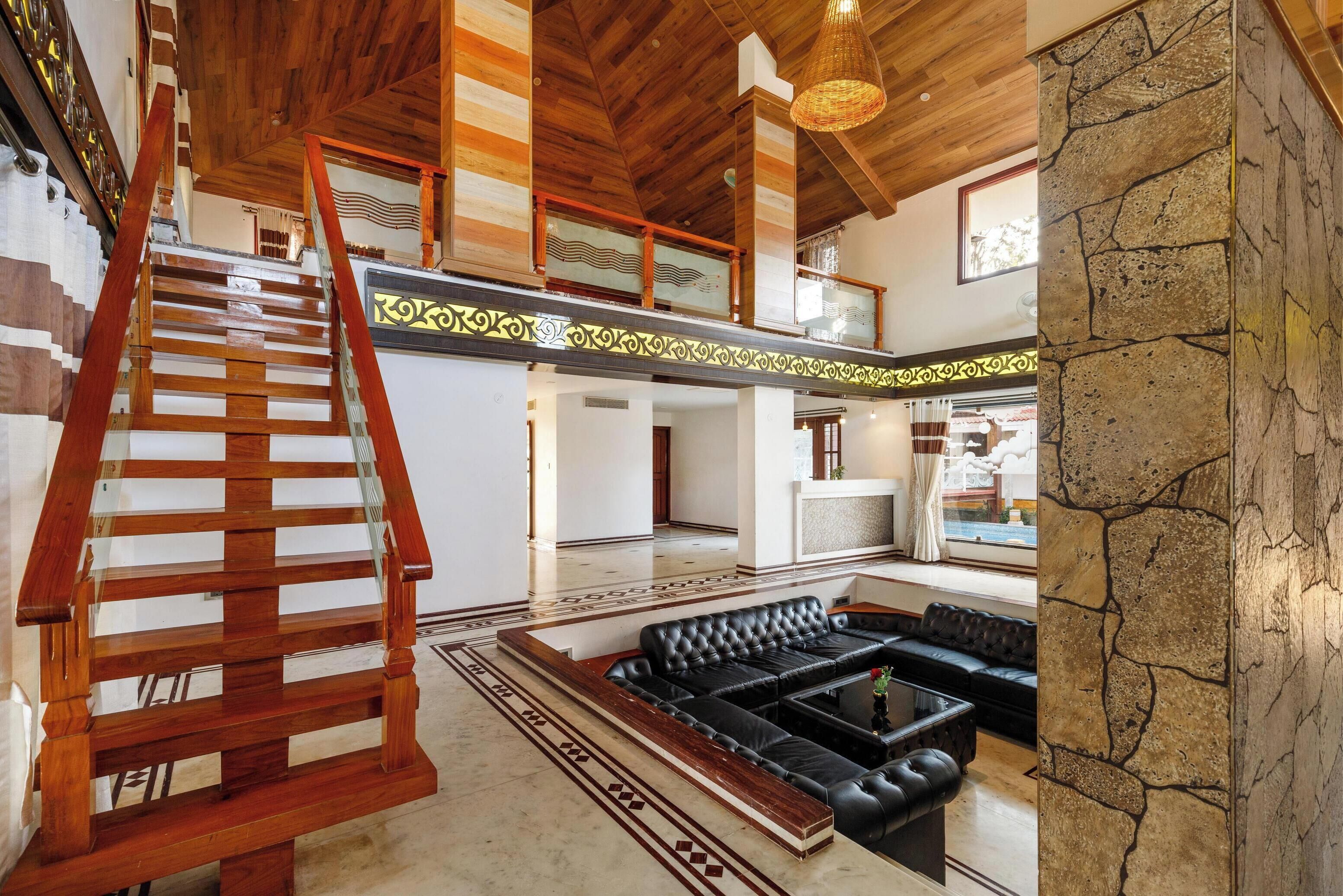 A spacious living area with a wooden staircase, a black leather sofa, and a stone accent wall.