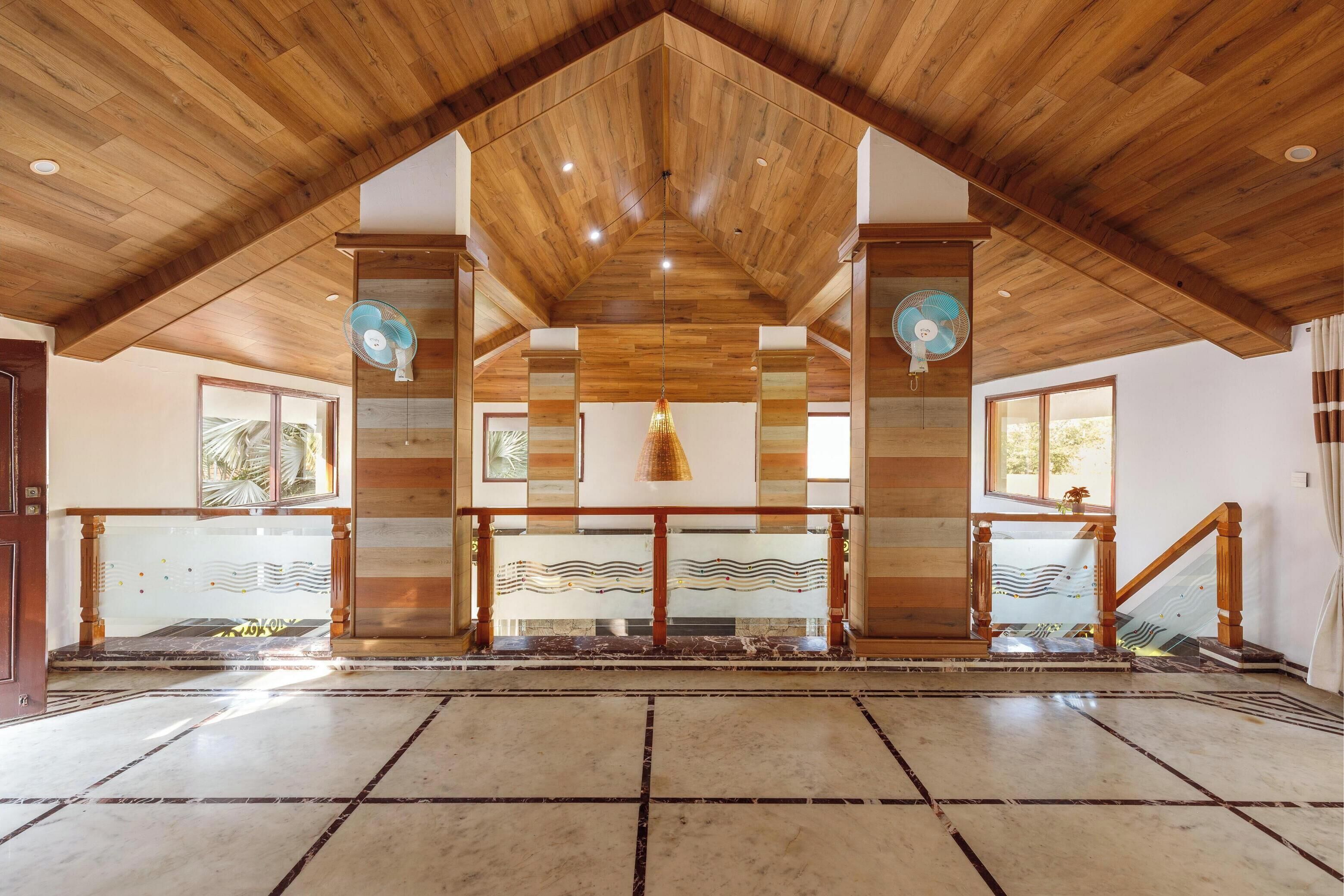 A spacious interior with a high wooden ceiling, a central staircase, and a patterned floor.