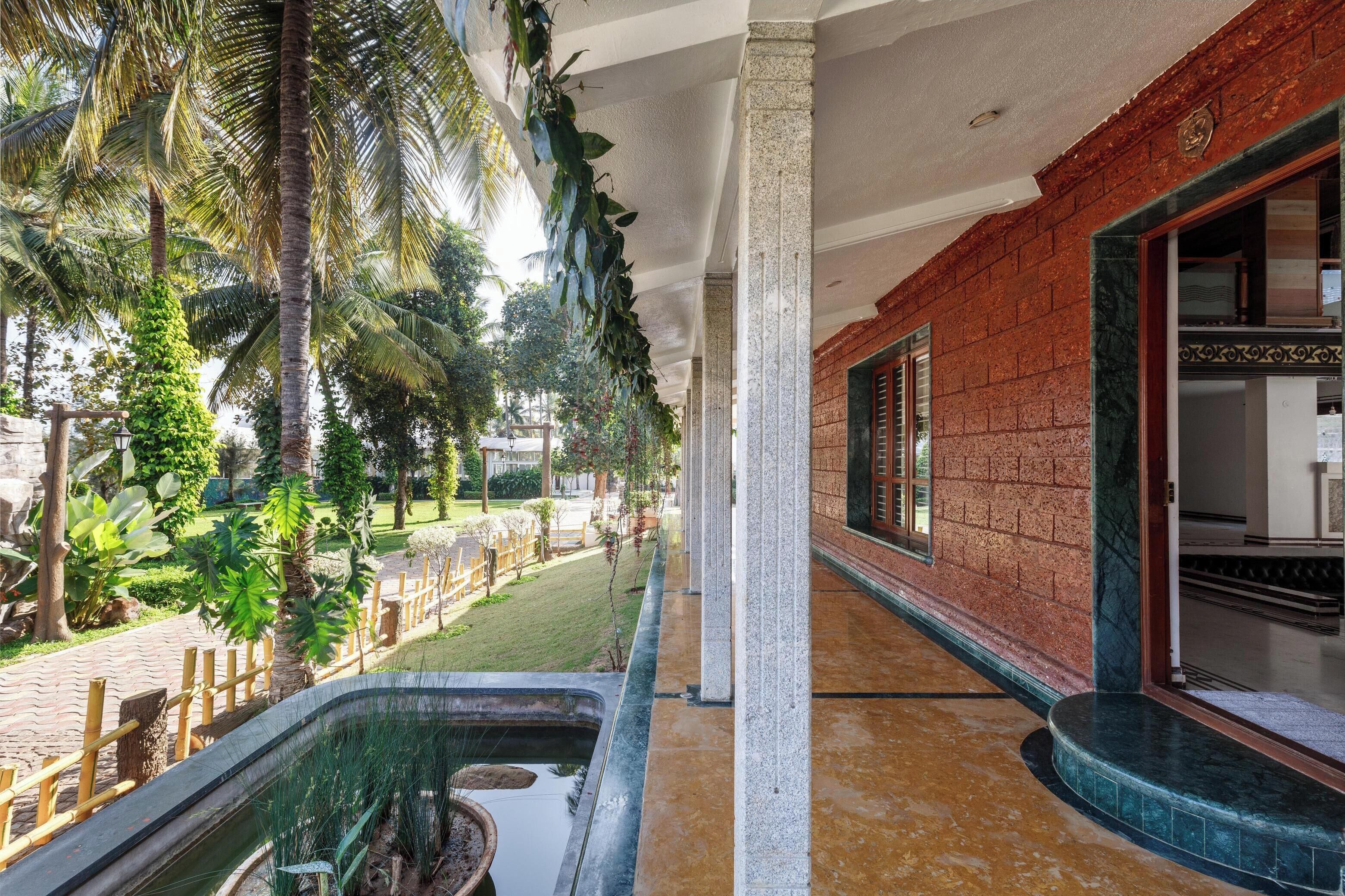 Um corredor com parede de tijolos, uma janela e vista para um jardim com palmeiras e um espelho d'água.