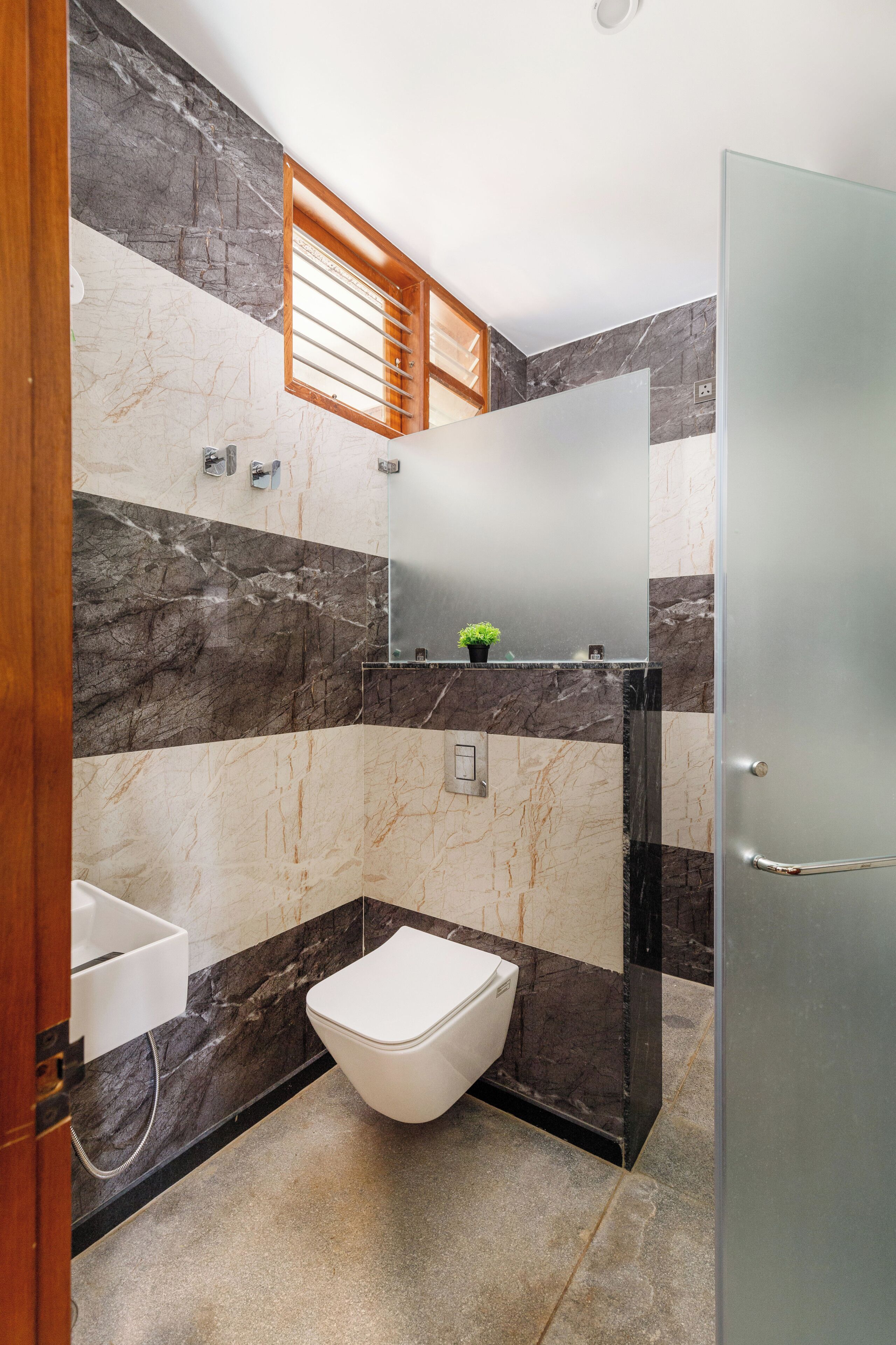 Et moderne badeværelse med en marmorvæg, et hvidt toilet, en vask og et spejl.