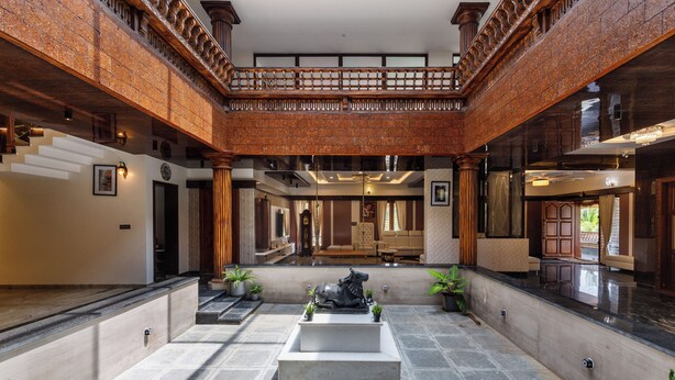 Un vaste atrium doté d’une fontaine centrale, d’un balcon en bois et offrant une vue sur l’intérieur.
