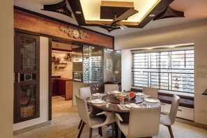 A dining area with a round table set for six, surrounded by chairs. A large window provides a view of the cityscape. - Serenity Villa by Red Olive (Bengaluru)