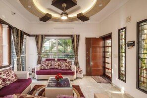 A living room with a sofa set, a coffee table with flowers, and a large window with curtains. - Serenity Villa by Red Olive (Bengaluru)