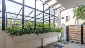 A covered outdoor area with a glass roof, a planter with green plants, a black metal gate, and a tiled floor. - Serenity Villa by Red Olive (Bengaluru)