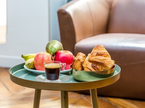 A table with a green tray holding a cup of coffee, apples, bananas, and croissants. - Merveil Luxury Suites AboukirI-II-III-IV (Paris)