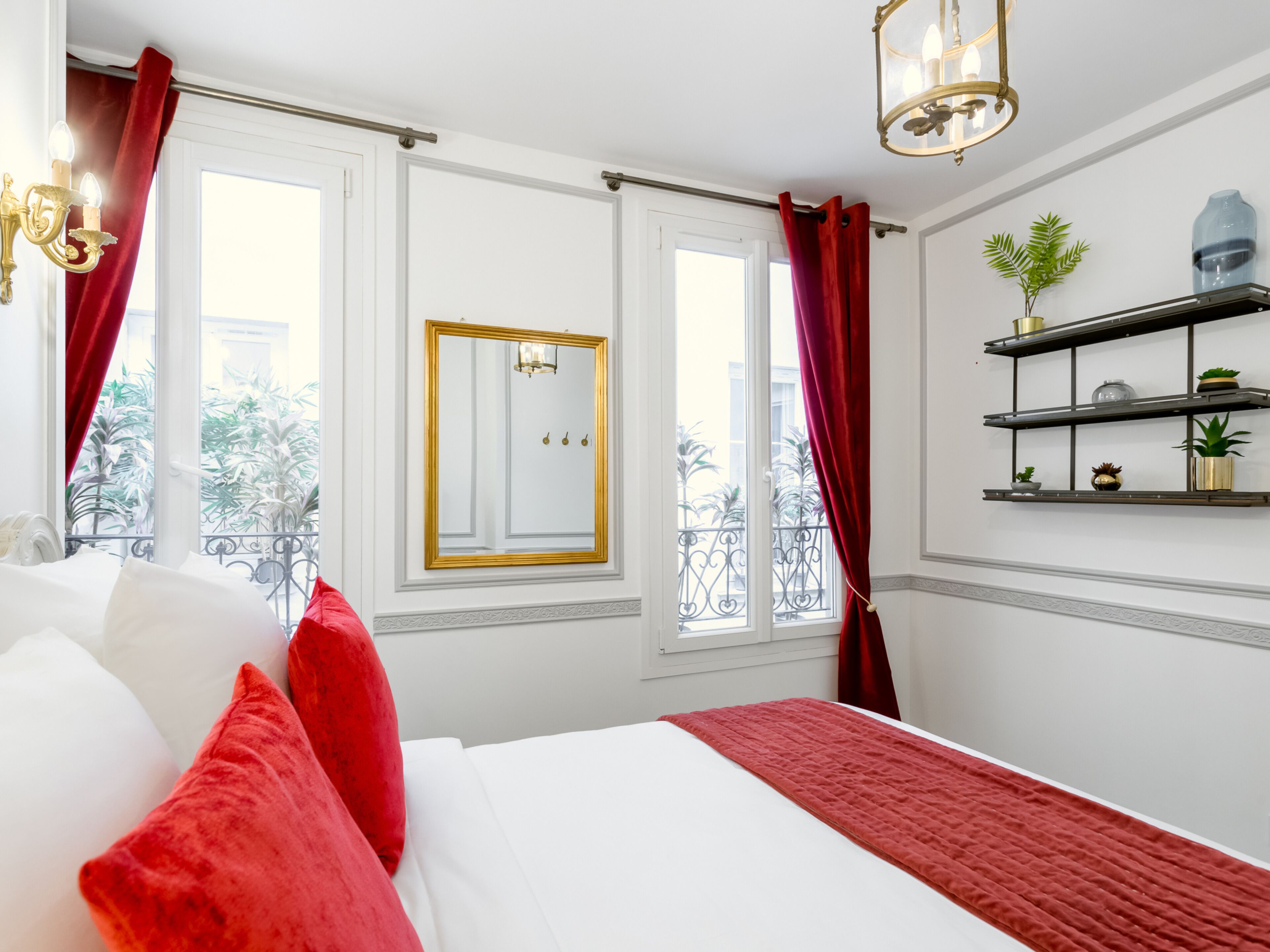 Habitación de hotel con una cama grande, cortinas rojas, un espejo y vistas al balcón.
